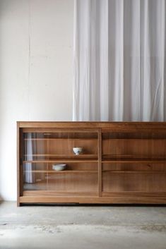 a wooden entertainment center with glass doors and shelves on the front, against a white curtain