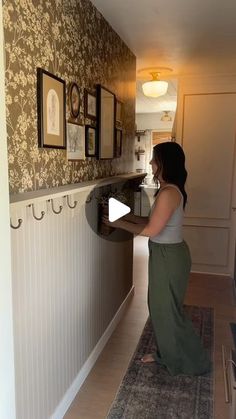 a woman standing in front of a kitchen counter next to a wall with pictures on it