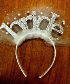 a headband with the word bride written on it and pearls in the middle, sitting on a wooden surface