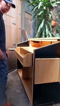 a man standing in front of a wooden cabinet with drawers on wheels and an open door