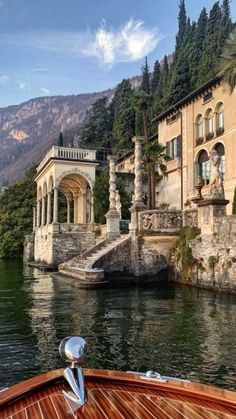 a boat traveling down a river next to a large building on top of a hill