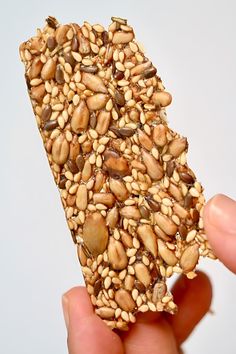 a hand holding up a piece of food with nuts on it's side and seeds all over the top