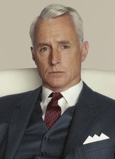 a man in a suit and tie sitting on a white chair with his arms crossed