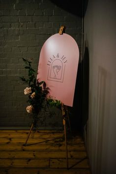 a pink sign sitting on top of a wooden easel next to a brick wall