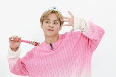 the young man is wearing a pink sweater and holding a toothbrush in his hand