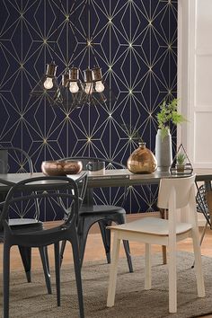 a dining room table with chairs and a vase on top of it, in front of a blue geometric wallpaper