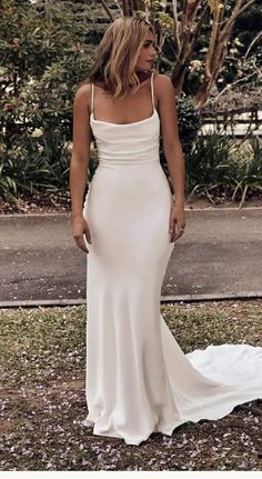 a woman wearing a white dress standing in the grass with her back to the camera