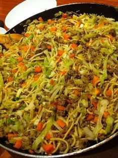 a pan filled with noodles and vegetables on top of a wooden table