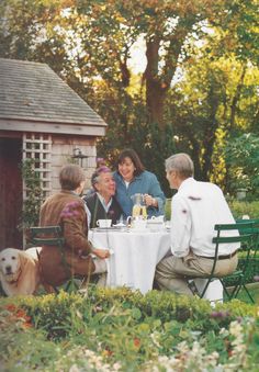 people sitting at a table in the middle of a garden with a dog looking on