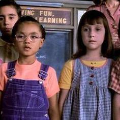 three children standing in front of a chalkboard with writing on the wall behind them