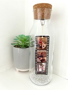 a glass bottle with some pictures in it next to a potted plant