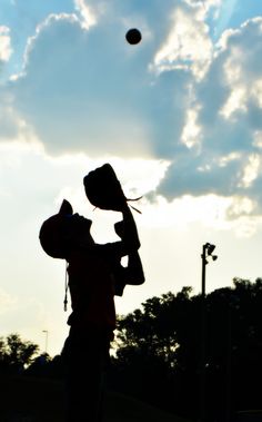 a person holding a baseball mitt in front of a cloudy sky with the sun behind them