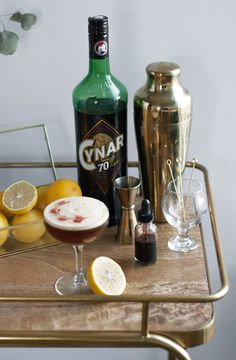 a table topped with drinks and lemons next to a metal shaker on top of a wooden table