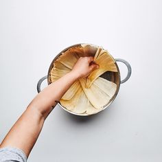 a person's hand reaching into a pot filled with food on top of a table