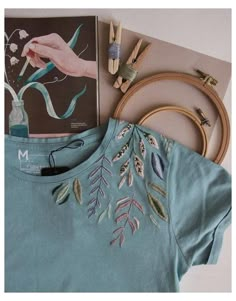 a t - shirt with embroidery on it next to some crafting supplies and a book