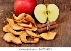 an apple, cinnamon sticks and apples on a wooden table with one cut in half