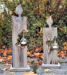 two wooden sculptures sitting next to each other on top of a gravel ground with leaves around them