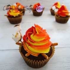 cupcakes decorated with orange and yellow frosting on top of wooden table next to marshmallows