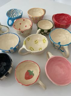 many bowls and spoons with faces painted on them sitting on a white table top