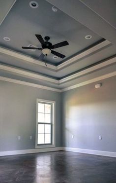 an empty room with a ceiling fan and two windows in the corner, all painted gray