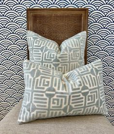 two blue pillows sitting on top of a chair next to a wallpapered wall