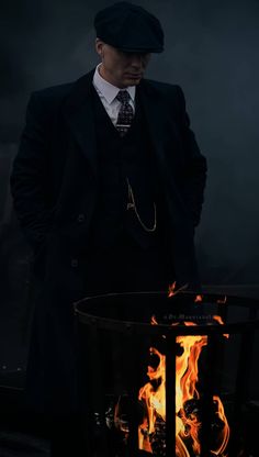 a man in a suit and tie standing next to a fire pit with flames on it