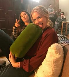 two women are sitting on the couch and one is holding a pillow