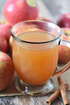 a glass mug filled with apple cider next to cinnamon sticks