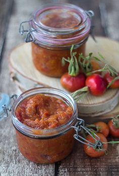 three jars filled with tomato sauce sitting on top of a wooden table next to tomatoes