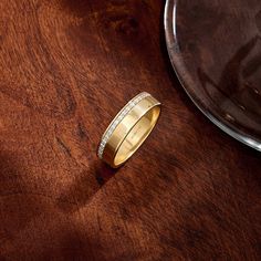 a gold wedding band with pave set diamonds sits on a wooden table next to a plate