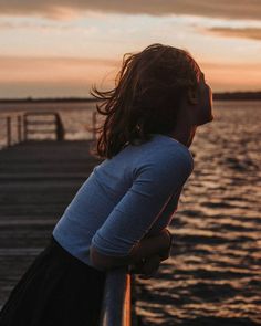 a girl standing on a pier looking at the water with her eyes closed and hair blowing in the wind