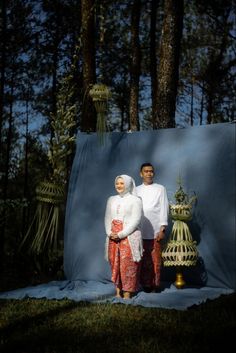 two people standing next to each other in front of trees