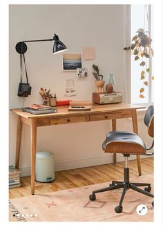 a desk with a chair, lamp and other items on it in front of a window