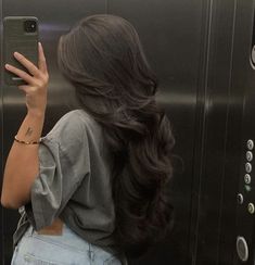 a woman taking a selfie with her cell phone in an empty elevator stall while wearing denim overalls