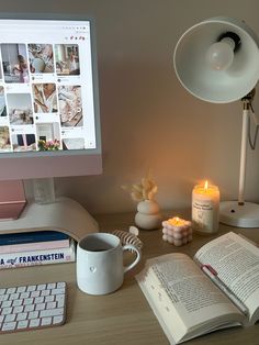 an open book on a desk next to a computer monitor and keyboard with a lit candle