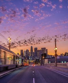 a train traveling down the tracks in front of a city skyline at dusk with clouds