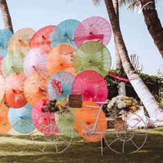 many colorful umbrellas on display in front of some palm trees and a white cart