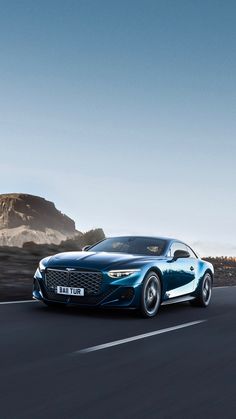 a blue sports car driving down the road in front of some mountains and sand dunes