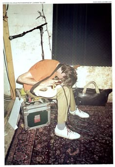 a young man sitting on top of a chair next to an old tv and guitar