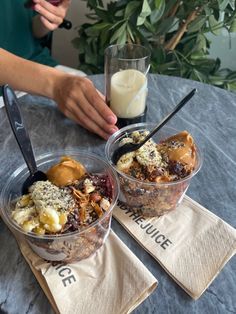 two desserts in plastic containers with spoons on the table next to each other