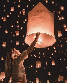 a woman holding up a lantern in the air with lots of lanterns floating above her