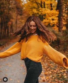 a woman in yellow sweater and black jeans walking down a path with her arms outstretched