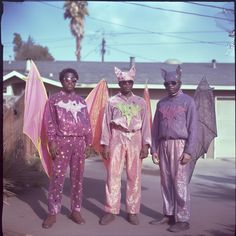 three black men dressed in pink and purple clothing standing next to each other on the street