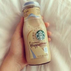 a hand holding a bottle of starbucks frappuccino on top of a bed