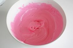 a white bowl filled with pink icing on top of a table