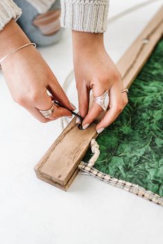 a woman is working on a piece of art with her hands and nails, while another person sits in the background