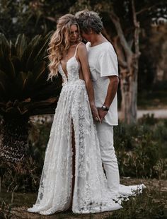 a man and woman standing next to each other in front of some trees with their arms around each other