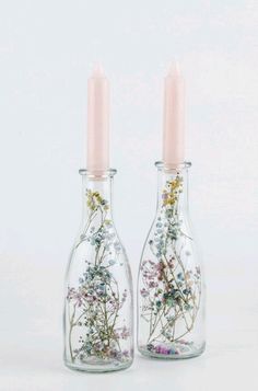 two glass bottles with flowers in them sitting next to each other on a white surface