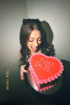 a woman holding a heart shaped cake with the words f k i m e s on it