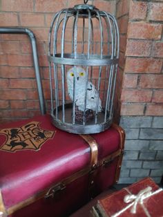 a white bird in a cage sitting on top of two red suitcases next to a brick wall